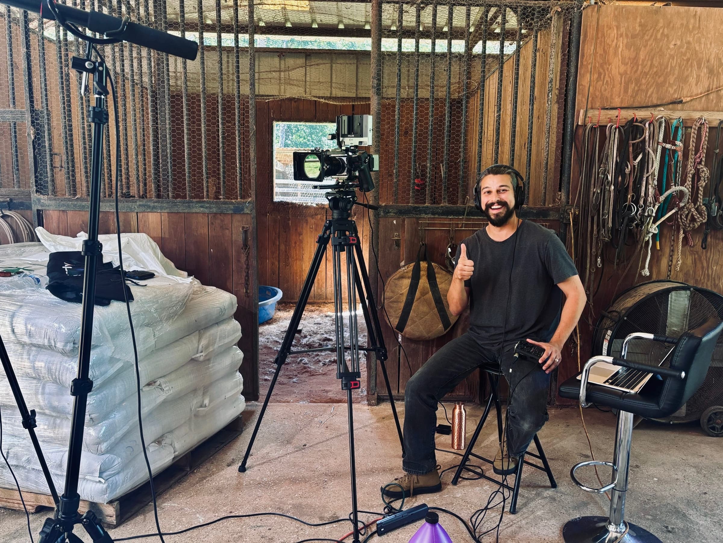 Nick Garza smiling and giving a thumbs-up beside a cinema camera and boom mic in a barn production setting