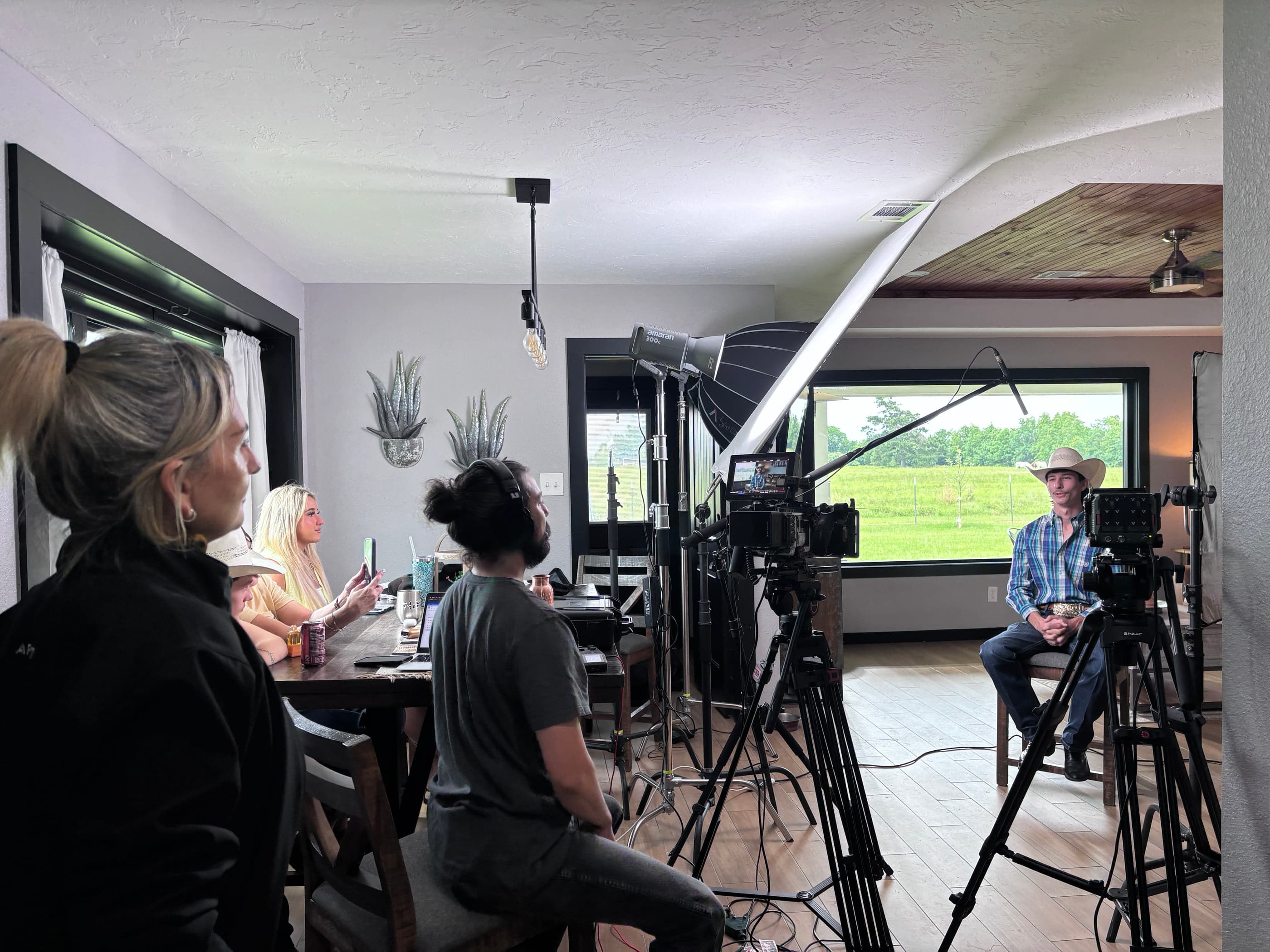 A full production crew, lighting, and camera set up for an interview inside a barn overlooking pasture